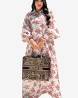 A woman modeling a long-sleeved, high-neck maxi dress with a pink palm tree pattern on a white background, holding a Christian Dior tote bag.
