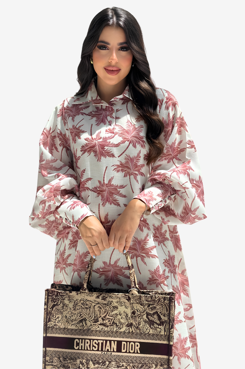 A woman wearing a white long-sleeve shirt with a pink palm tree pattern, holding a Christian Dior tote bag against a light gray background.