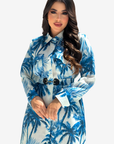 A woman modeling a long-sleeve collared shirt dress with a blue and white palm tree print, featuring a matching fabric belt with a black buckle, set against a plain light gray background.