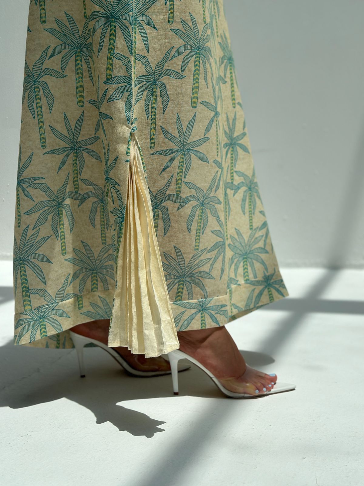 Palm Canopy Jalabiya close-up showing the pleated hem insert and teal palm print on cream linen blend fabric