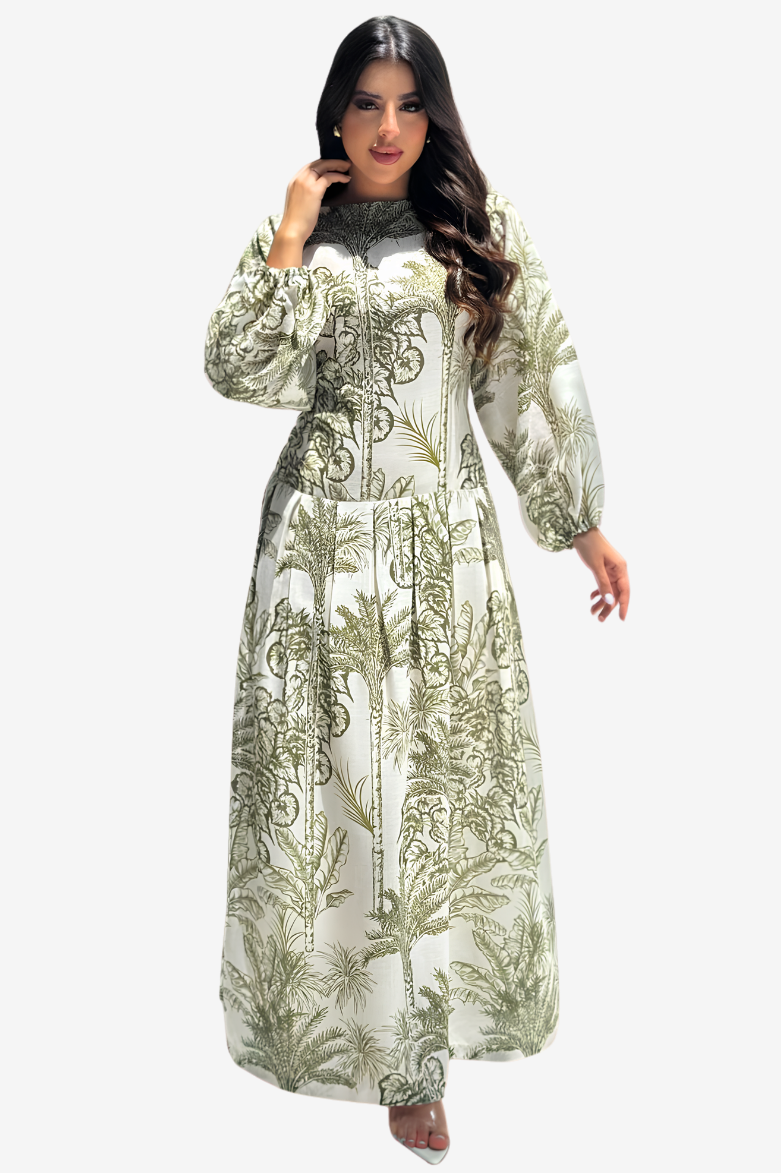 A woman modeling a long-sleeved maxi dress with a green botanical and scroll pattern on a white background, set against a plain light gray studio backdrop.