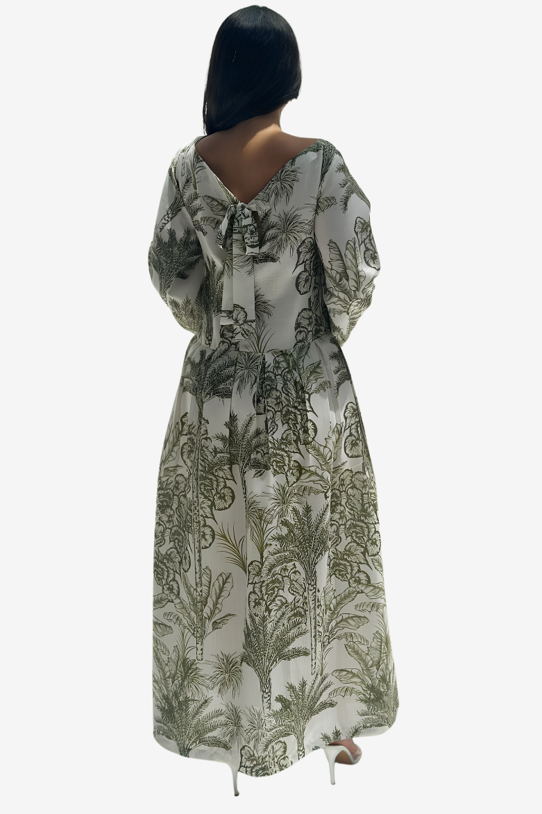 A woman viewed from the back wearing a long-sleeve maxi dress with a tie-neck detail and an all-over botanical print in olive green on a light beige background.