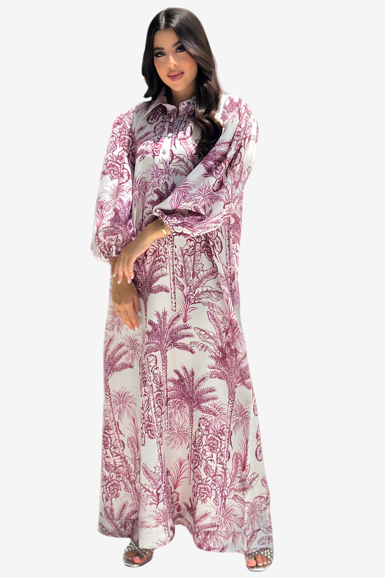 A woman modeling a long-sleeved maxi dress with a pink and white palm tree pattern, set against a plain light gray background.