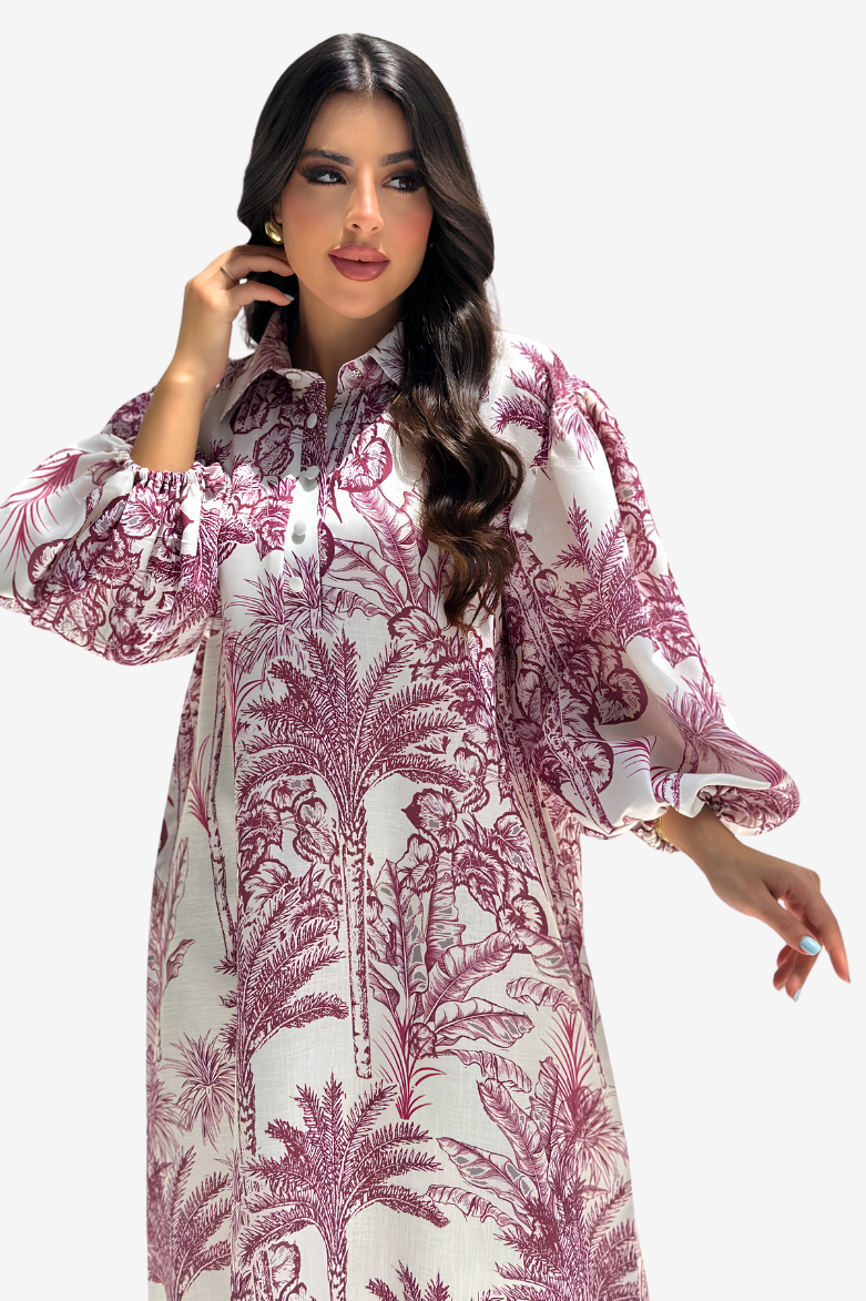 A woman modeling a long-sleeved white tunic dress with a dusty rose botanical palm tree print, set against a plain light gray background.