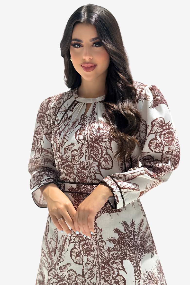 A woman modeling a long-sleeved dress with a brown botanical and palm tree print on a light beige background, set against a plain light gray studio background.