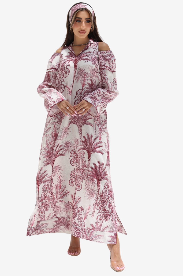 A woman modeling a long off-the-shoulder maxi dress with a pink and white botanical pattern, paired with a matching headband and clear high-heeled sandals, set against a plain light gray background.