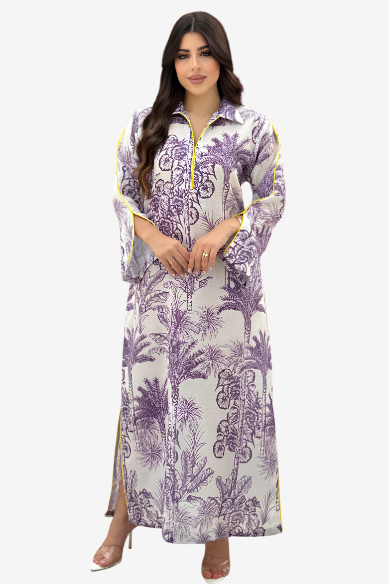 A woman modeling a long-sleeved maxi dress with a purple palm tree pattern on a white background, featuring yellow piping details along the collar, cuffs, and side slits.