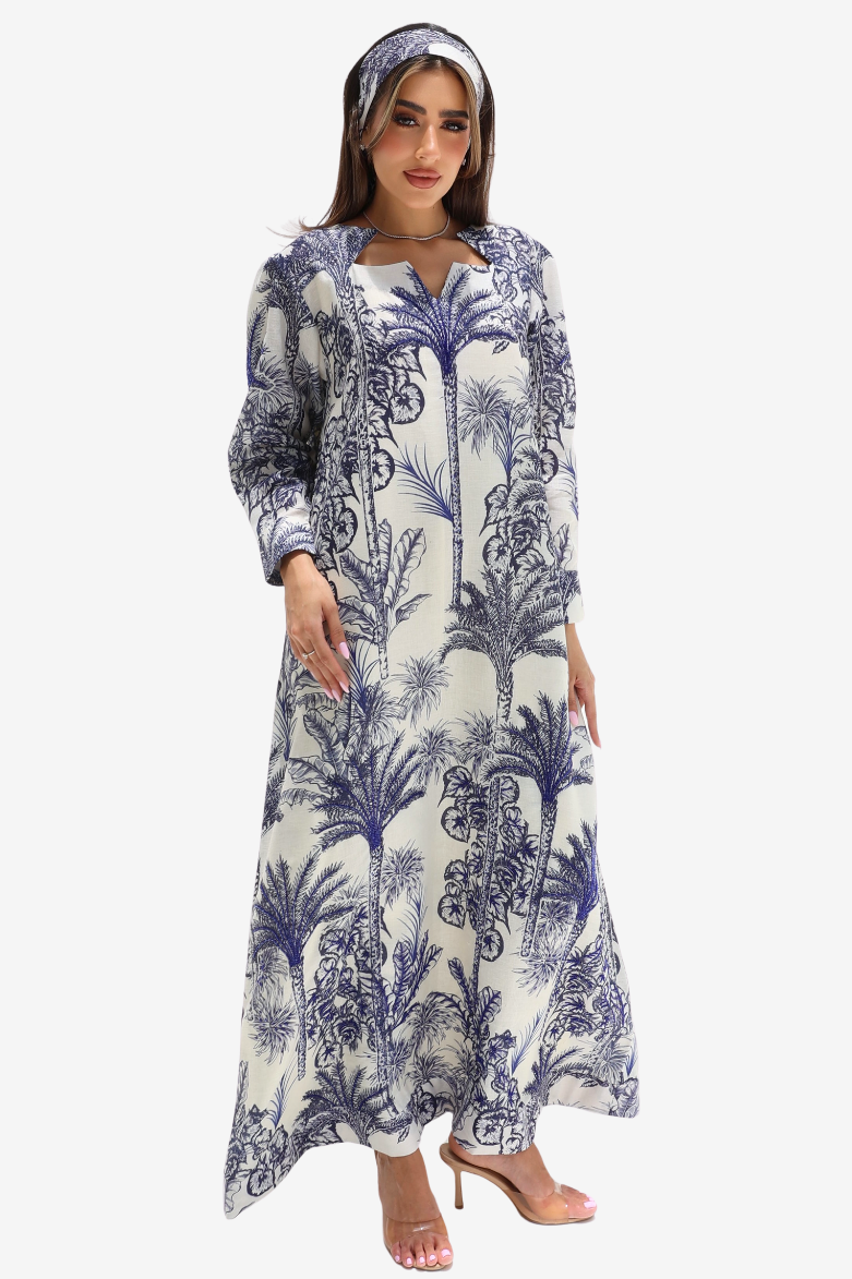 A woman modeling a long-sleeved maxi dress with a blue and white palm tree pattern, paired with a matching headband and nude high-heeled sandals, set against a plain light gray background.