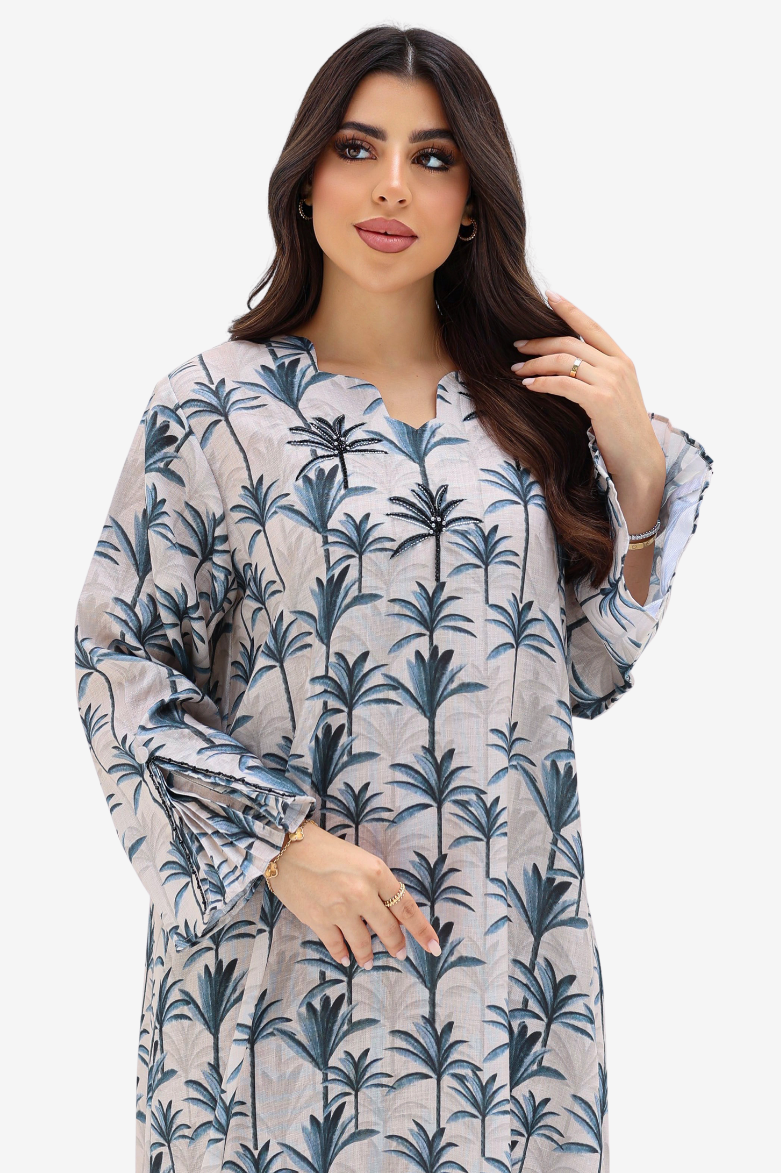 A woman modeling a long-sleeve tunic dress with a blue palm tree print on a light gray background, set against a plain light gray studio backdrop.