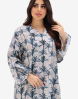 A woman modeling a long-sleeve tunic dress with a blue palm tree print on a light gray background, set against a plain light gray studio backdrop.
