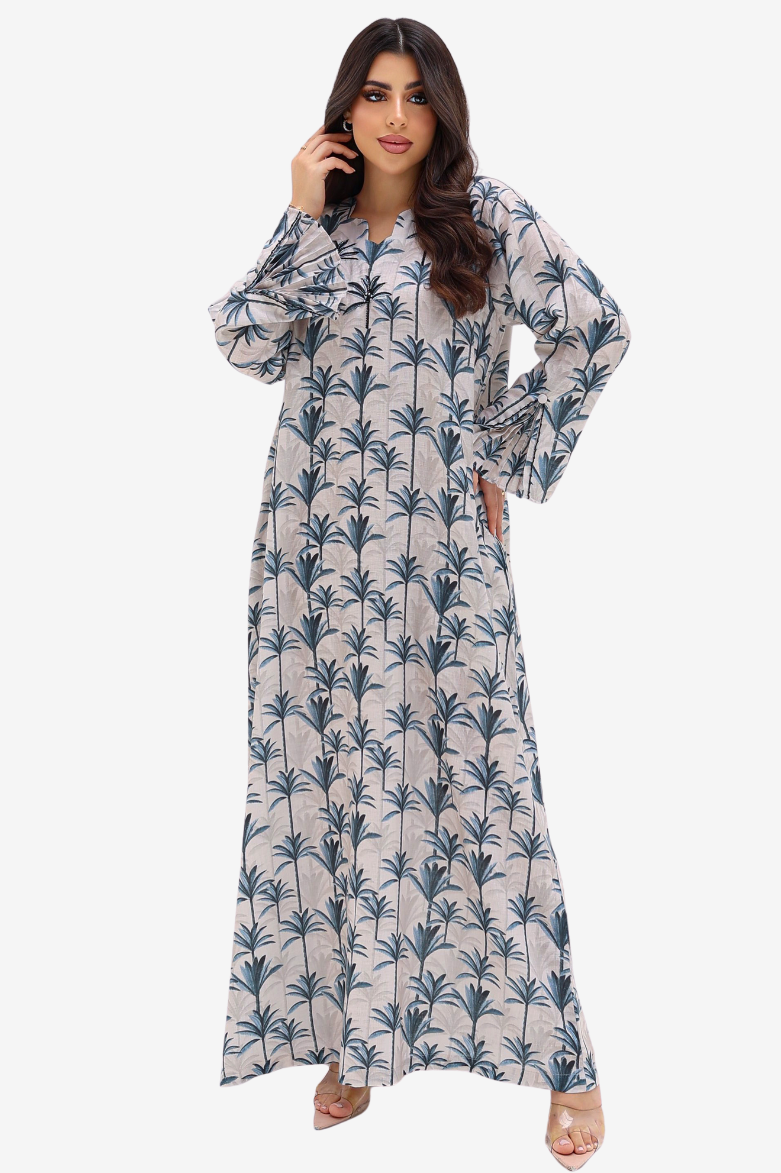 A woman modeling a long-sleeved maxi dress with a blue palm tree pattern on a light beige background, set against a plain light gray studio backdrop.