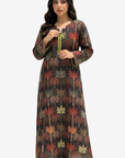 A woman modeling a long-sleeved, floor-length tunic dress with a dark brown base and an all-over palm tree print in red, green, and beige, featuring a lime green drawstring at the neckline.