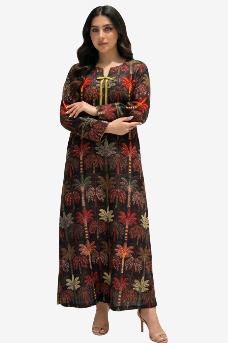 A woman modeling a long-sleeved maxi dress with a dark brown base and an all-over palm tree print in red, green, and beige. The dress features a round neckline with a yellow tie detail at the center chest.