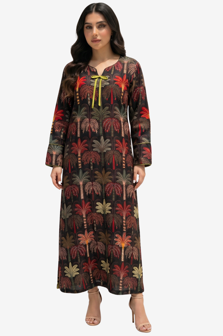 A woman modeling a long-sleeved maxi dress with an all-over palm tree print on a black background, featuring a yellow tie at the neckline, set against a plain light gray studio background.