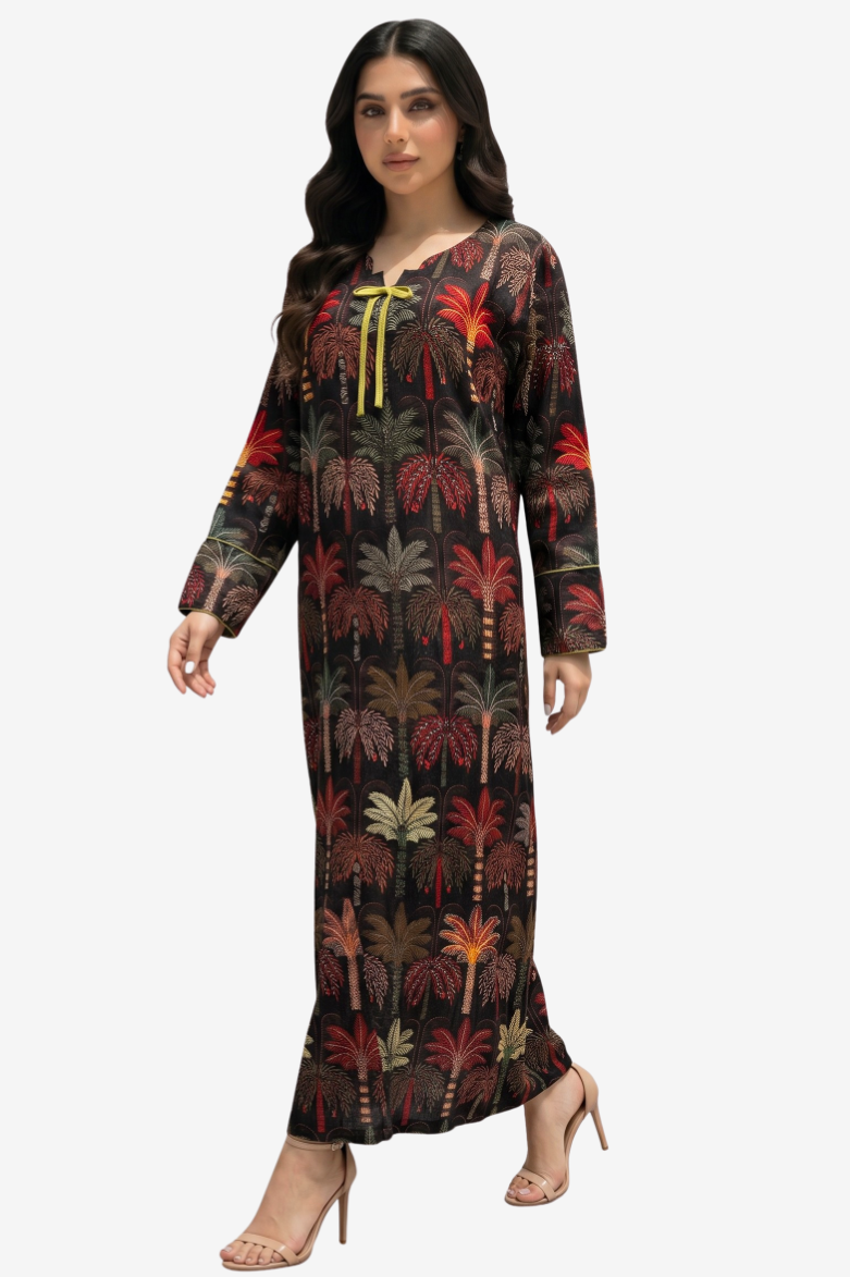 A woman modeling a long-sleeved maxi dress with a tropical palm tree print in red, green, and brown tones on a black background, featuring a yellow tie detail at the neckline, set against a plain light gray background.