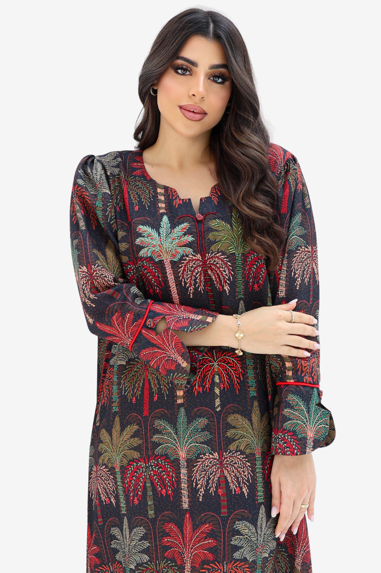 A woman modeling a long-sleeve tunic dress with a dark background and a colorful palm tree print in red, green, and beige, set against a plain light gray background.