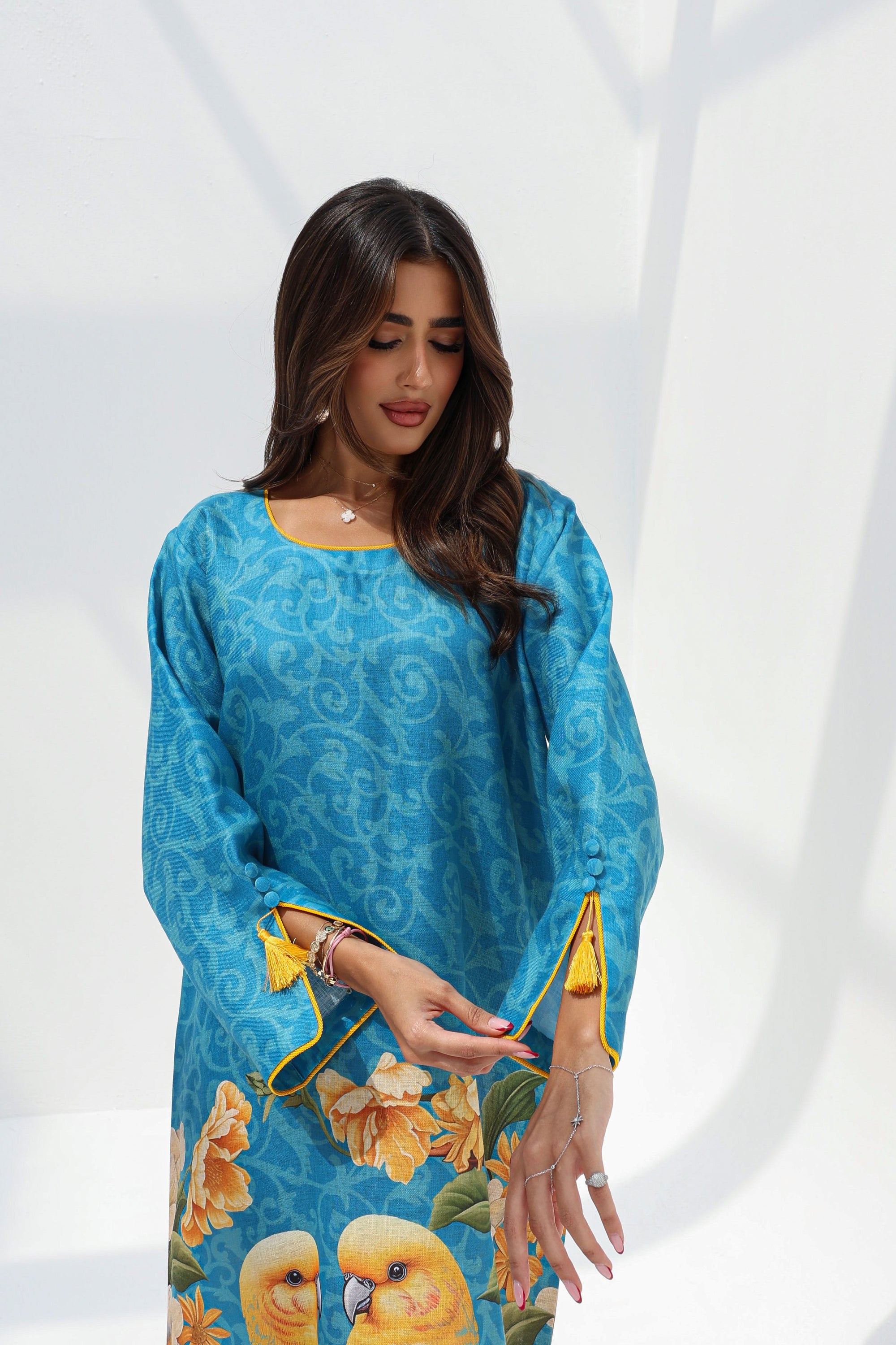 Three-quarter portrait of turquoise printed jalabiya with round neckline and tassel-detailed cuffs