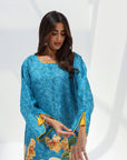 Three-quarter portrait of turquoise printed jalabiya with round neckline and tassel-detailed cuffs