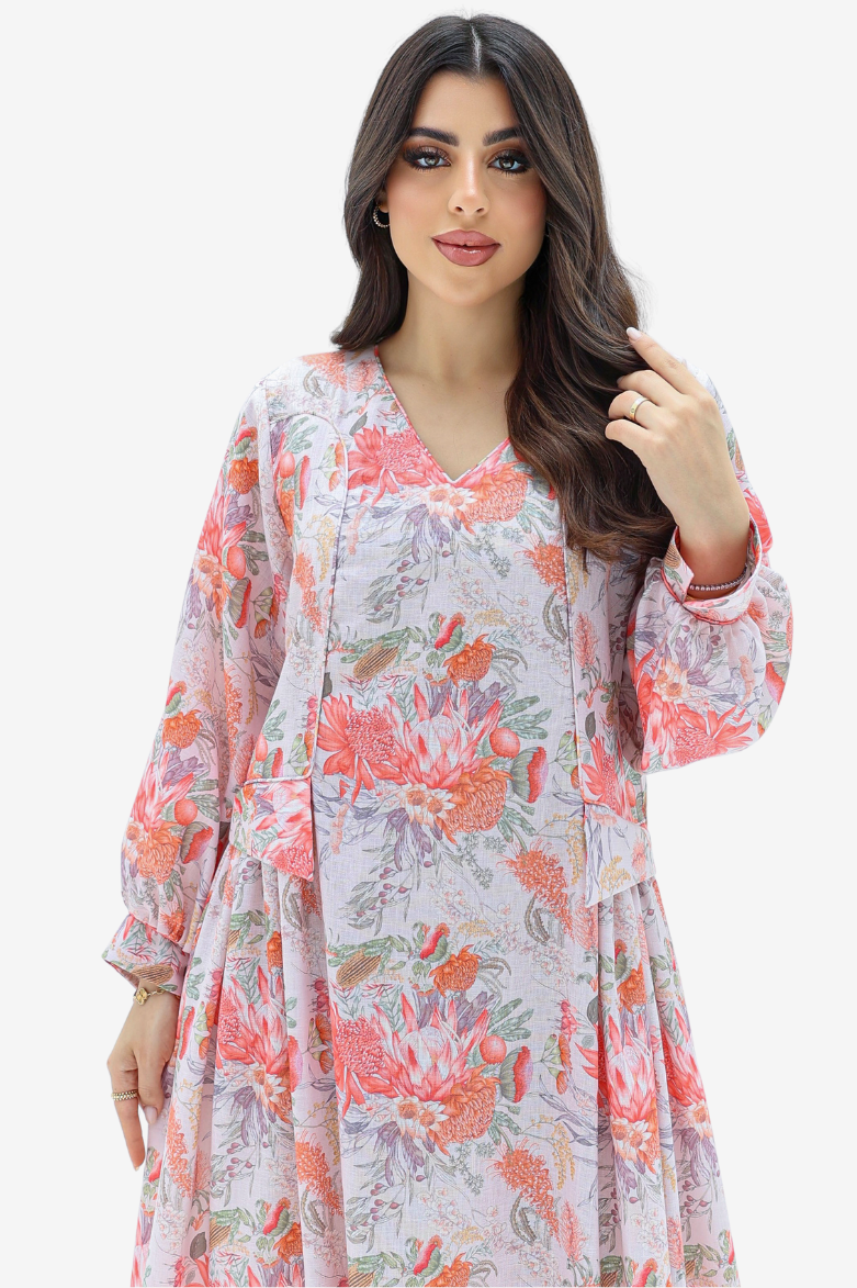 A woman modeling a long-sleeve V-neck dress with a pink, orange, and green floral print on a light lavender background, set against a plain white studio backdrop.