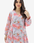 A woman modeling a long-sleeve V-neck dress with a pink, orange, and green floral print on a light lavender background, set against a plain white studio backdrop.