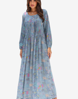 A woman modeling a long-sleeve, floor-length blue maxi dress with a pastel multicolor floral print, set against a plain light gray background.