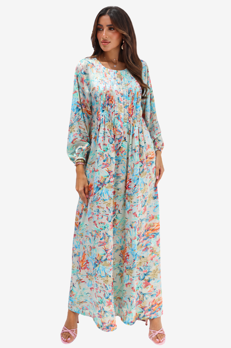 A woman modeling a long-sleeve maxi dress with a colorful abstract floral print on a light mint green background, paired with pink strappy heels, against a plain white studio background.