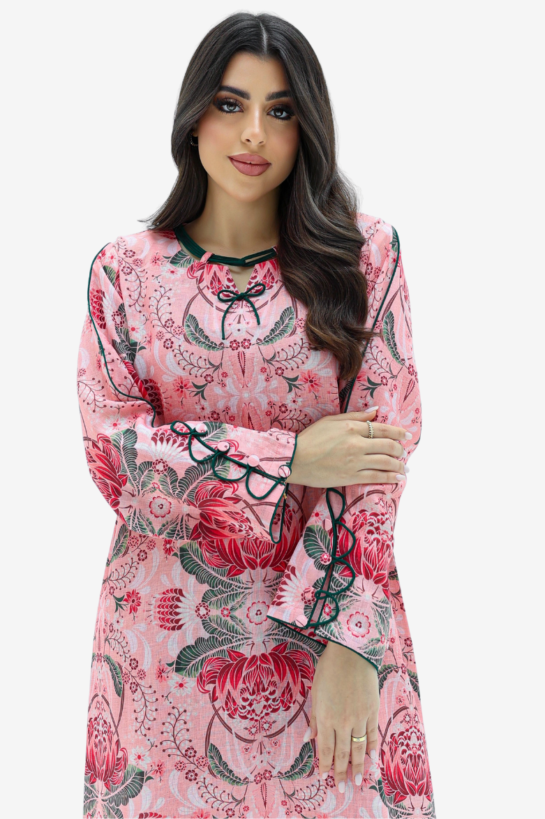 A woman modeling a pink long-sleeve tunic dress with a red and green floral pattern and black lace trim details, set against a plain light gray background.