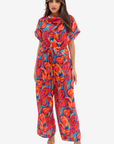 Prism Flow Sunset Abstract Linen Blend Jumpsuit by Gharza Couture featuring a vibrant multicolour abstract print, draped neckline, tie waist and wide-leg silhouette.