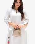 A woman modeling a white long-sleeve tunic dress with a split neckline and black palm tree prints near the hem, holding a small beige handbag against a plain light background.