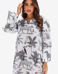A woman modeling a white long-sleeve tunic dress with a black safari animal and palm tree print, featuring a split neckline and flared sleeves.