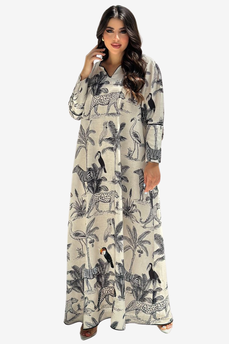 A woman modeling a long-sleeved, button-front maxi dress with a beige background and a black safari-themed print featuring palm trees, flamingos, zebras, and birds, set against a plain light gray background.