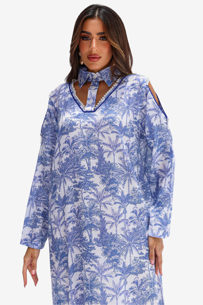 A woman wearing a long-sleeve blue and white tropical palm tree print dress with a keyhole cutout neckline and shoulder cutouts, shown against a plain light gray studio background.