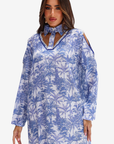 A woman wearing a long-sleeve blue and white tropical palm tree print dress with a keyhole cutout neckline and shoulder cutouts, shown against a plain light gray studio background.