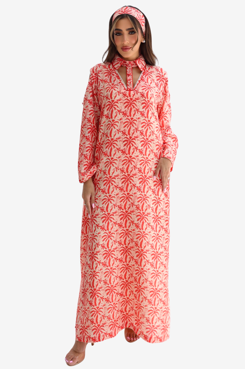 A woman modeling a long-sleeved maxi dress with a red palm tree pattern on a white background, paired with a matching headband, against a light gray studio background.