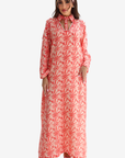 A woman modeling a long-sleeved maxi dress with a red palm tree pattern on a white background, paired with a matching headband, against a light gray studio background.
