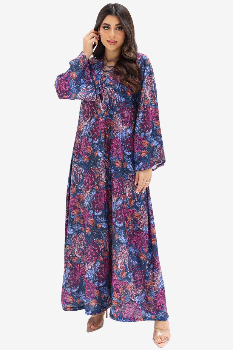 A woman modeling a long-sleeved, floor-length floral dress with a purple, blue, and pink pattern against a plain light gray background.