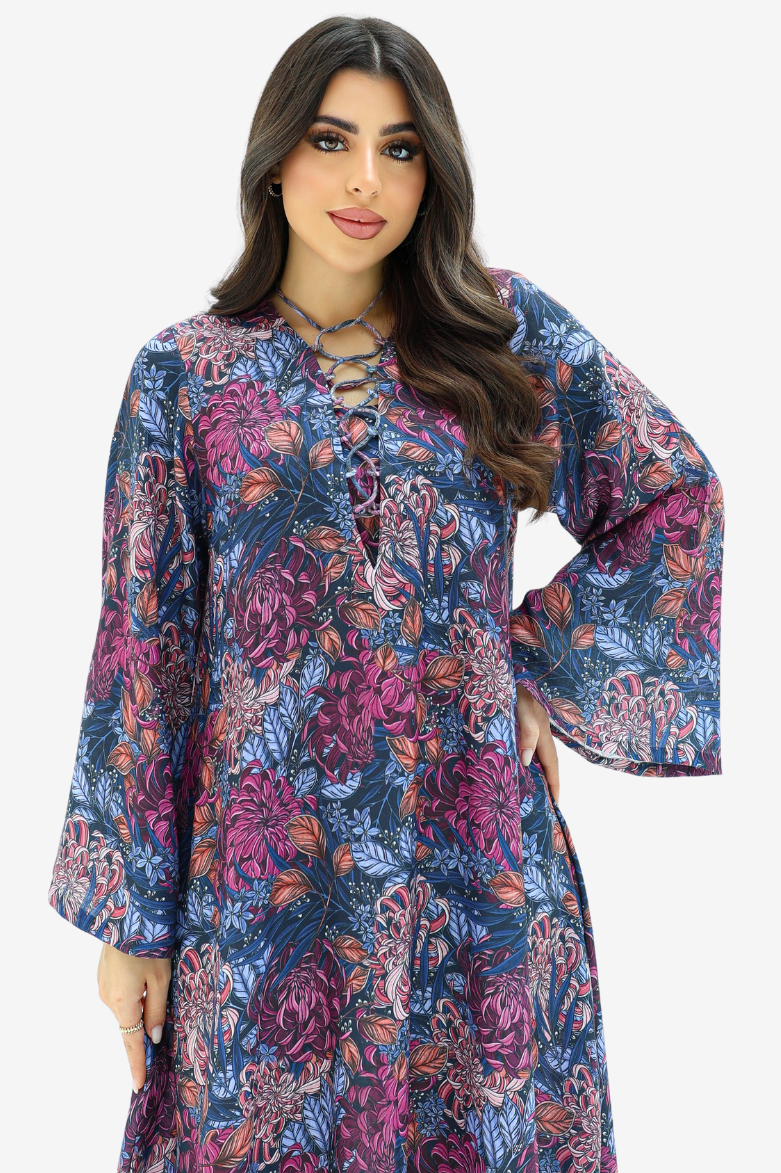 A woman modeling a long-sleeved bohemian-style tunic dress with a vibrant floral print in shades of purple, blue, and orange, featuring a lace-up neckline.