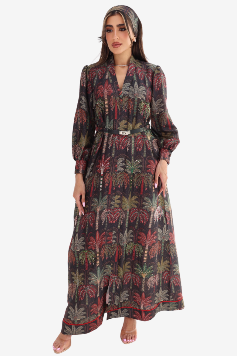 A woman modeling a long-sleeved maxi dress with a dark gray base and a colorful palm tree print in red, green, and beige, styled with a matching headscarf.