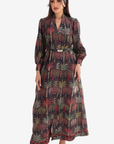 A woman modeling a long-sleeved maxi dress with a dark gray base and a colorful palm tree print in red, green, and beige, styled with a matching headscarf.