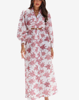 A woman modeling a long-sleeve white maxi dress with a pink floral print and a matching belt, set against a plain light gray background.