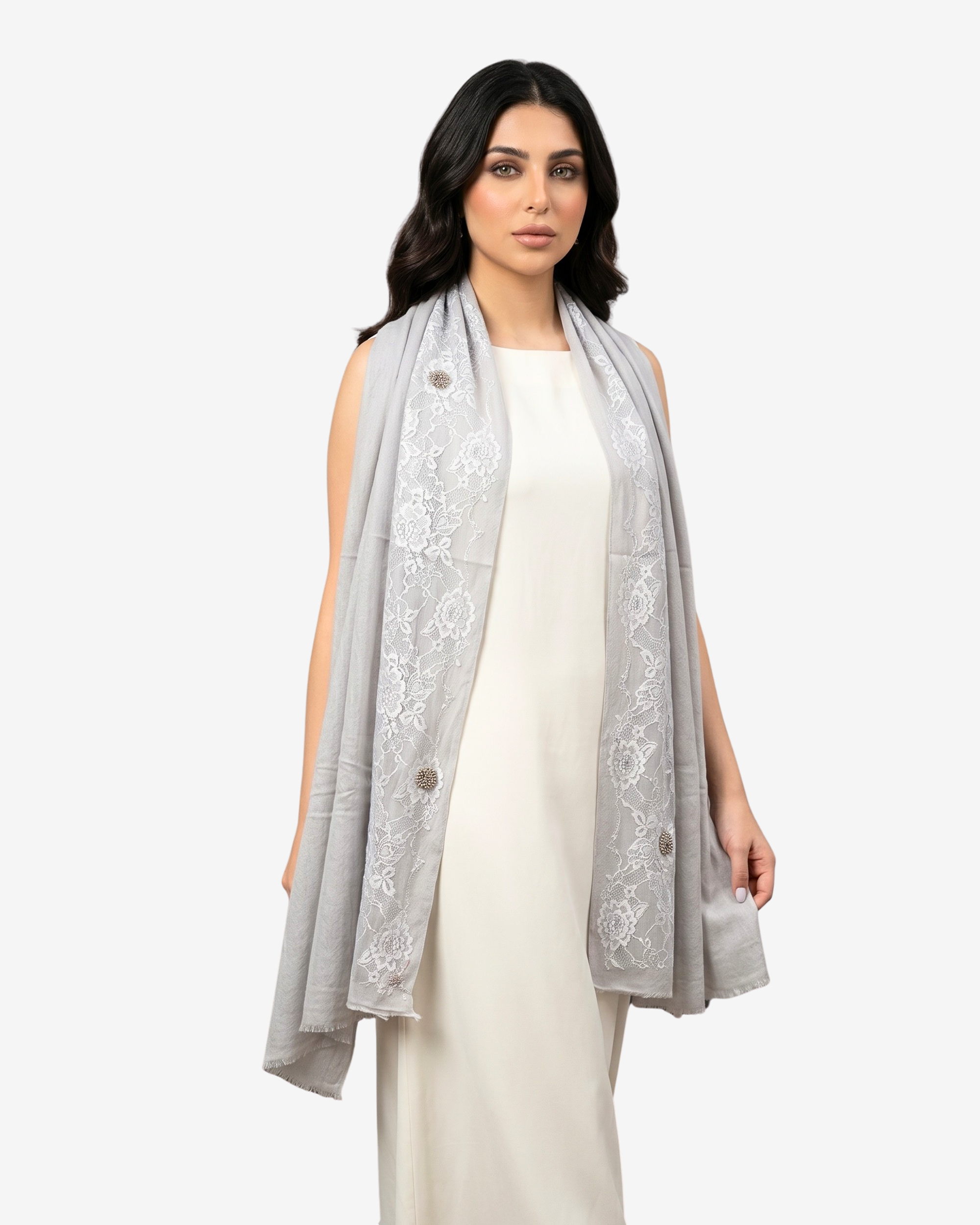 A woman modeling a light gray sleeveless shawl with white floral embroidery and decorative buttons, worn over a cream-colored dress against a plain light gray background.