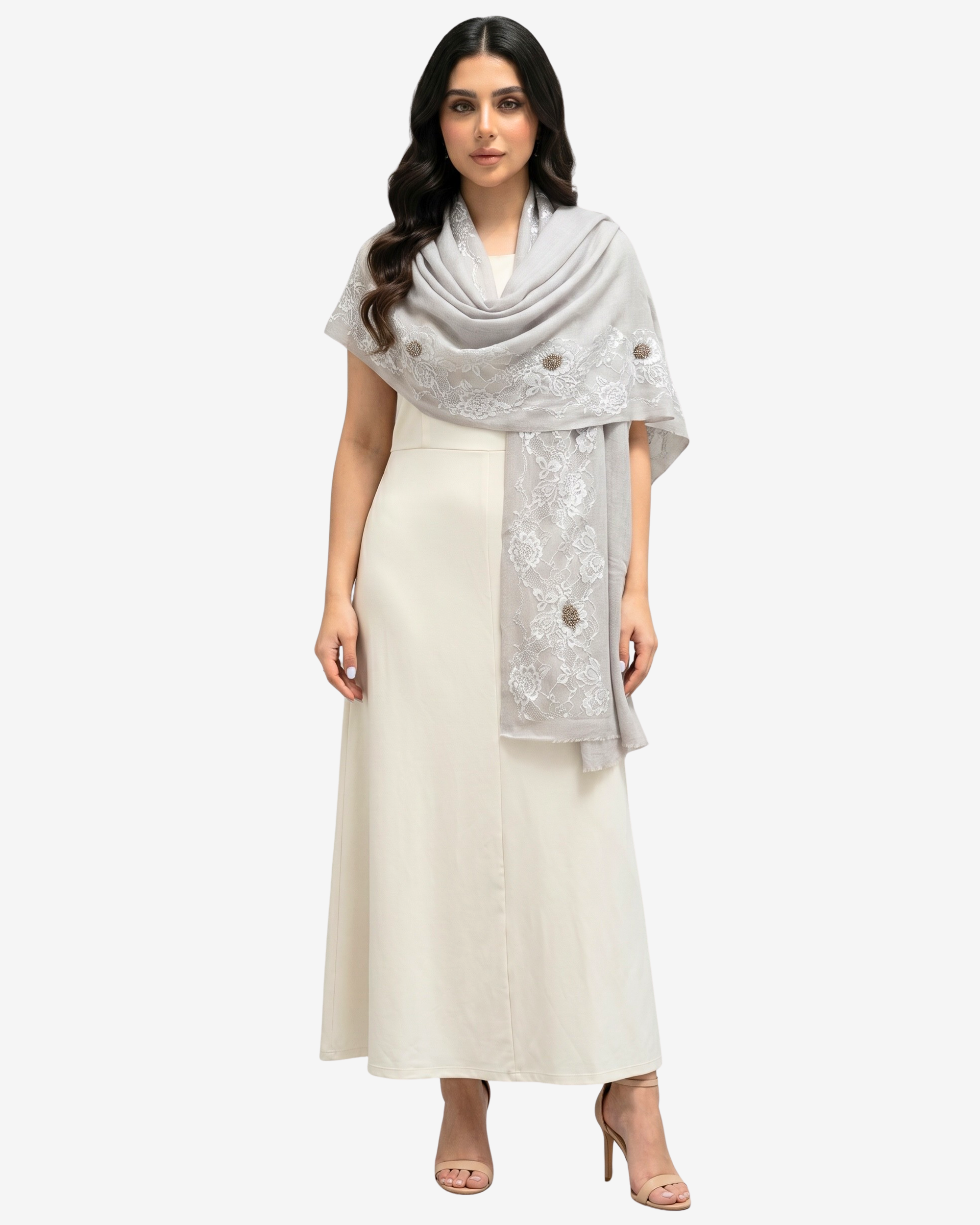 A woman modeling a light gray shawl with white floral embroidery and decorative buttons, worn over a cream-colored maxi dress against a light gray background.