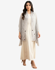 A woman modeling a light gray open-front cardigan with silver-gray floral embroidery over a cream-colored maxi dress, paired with nude high-heeled sandals, against a plain light gray background.