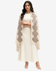 A woman modeling a cream-colored traditional outfit with a matching long skirt and crop top, draped with a sheer beige shawl featuring large gray floral lace patterns, set against a plain light gray background.