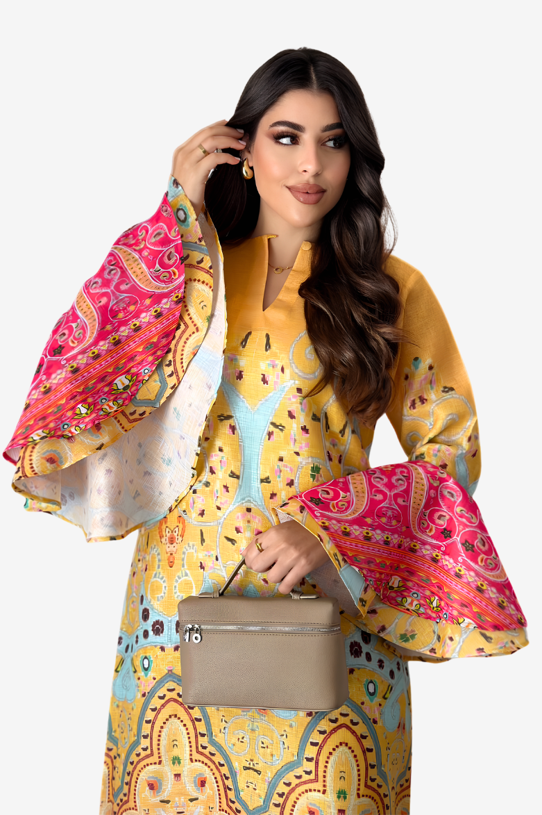 A woman modeling a vibrant yellow printed dress with dramatic bell sleeves featuring pink paisley patterns, holding a beige handbag against a light gray background.