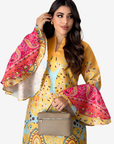 A woman modeling a vibrant yellow printed dress with dramatic bell sleeves featuring pink paisley patterns, holding a beige handbag against a light gray background.