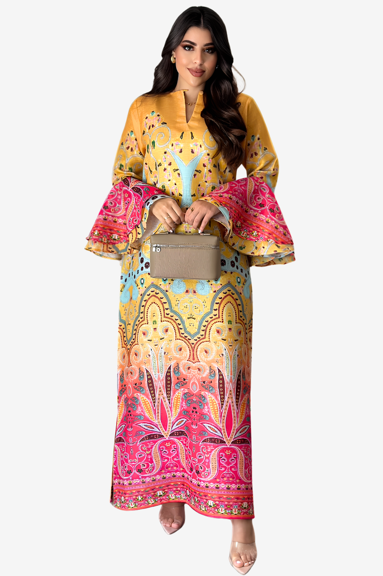 A woman modeling a long yellow and pink printed dress with bell sleeves and a geometric pattern, holding a small beige handbag against a light gray background.
