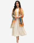 A woman modeling a lightweight, multicolored printed shawl draped over a cream-colored dress against a plain light gray background.