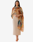 A woman modeling a beige midi skirt paired with a colorful abstract-printed shawl draped over her shoulders, set against a plain light gray background.