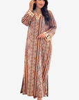 A woman modeling a long, loose maxi dress with a geometric tribal pattern in brown, beige, and orange tones, set against a plain light gray background.